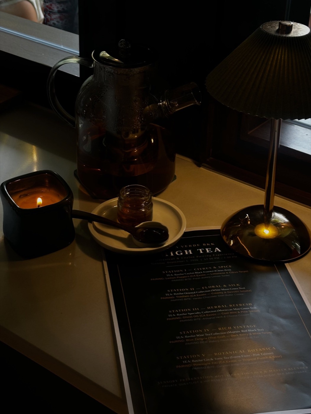 Their printed High Tea menu beside a candle and a glass teapot