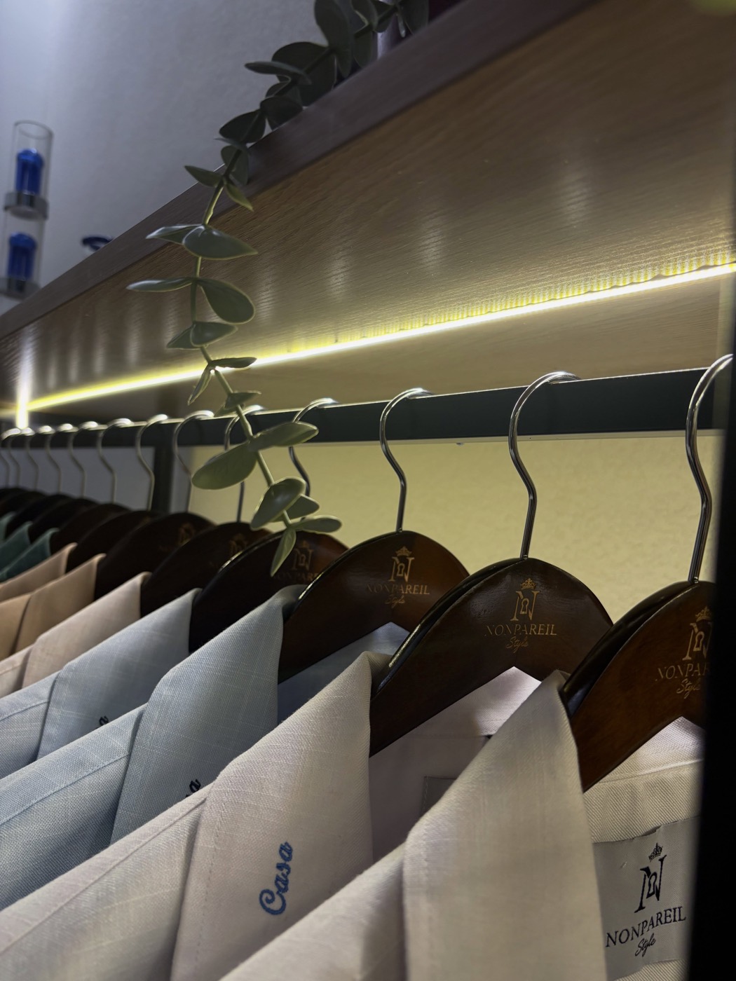 Linen-silk shirts on wooden hangers under a warm light strip